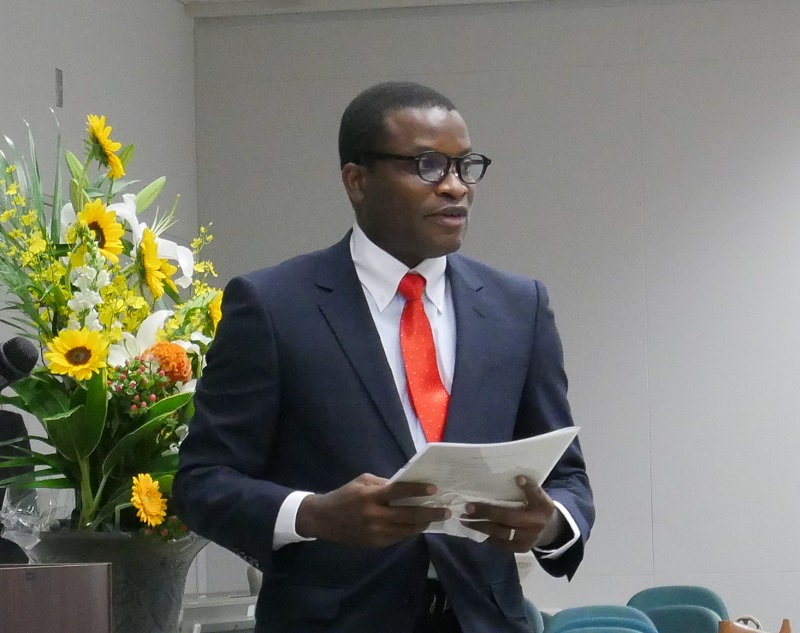 Young, handsome African man wearing a blue suit and red tie, and making a speech with paper in hand